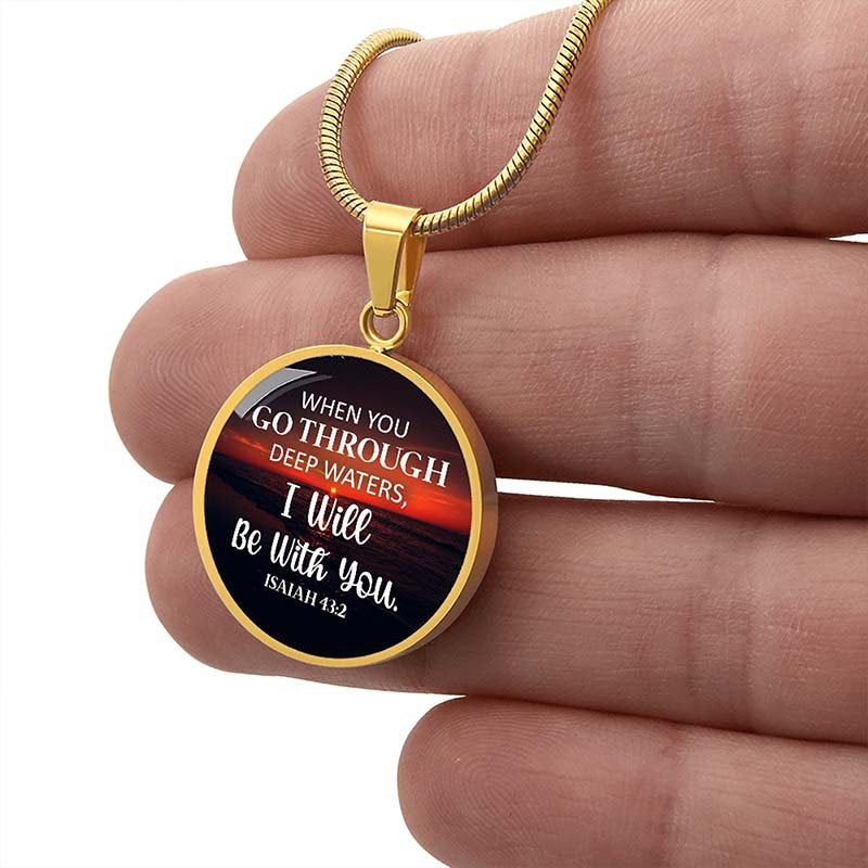 Gold round pendant with a bible verse on a black and red design held between fingers.