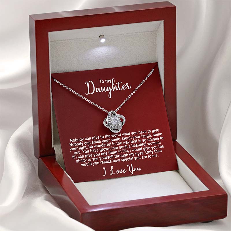 Silver knot necklace with a sentimental message card for a daughter on a red card displayed in a red wooden box against a light silk background.