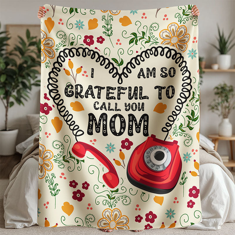 Blanket with a floral and red phone design and text 'I am so grateful to call you Mom' in a home setting.
