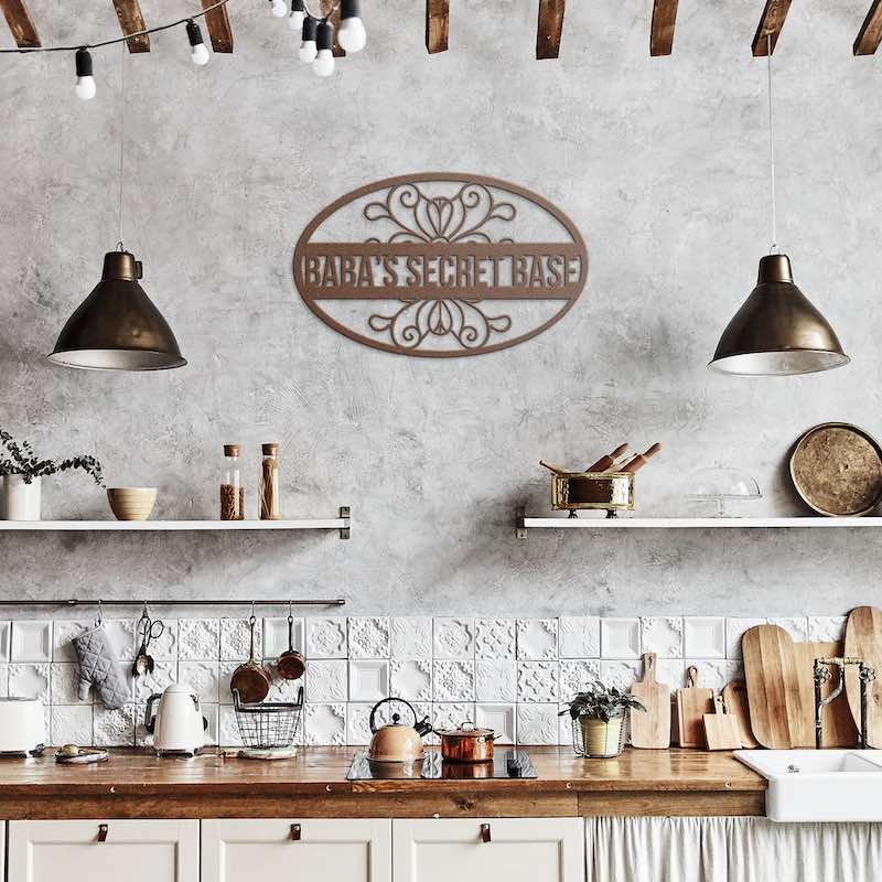 Kitchen interior with wooden countertops, and metal wall art with 'baba's secret base' text on it, between two hanging lights.