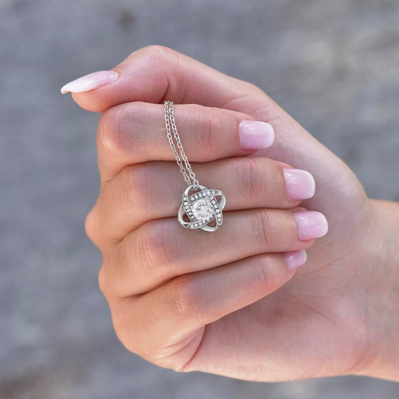 Knot necklace in white gold finish with a round cut centered zirconia stone held by a hand.