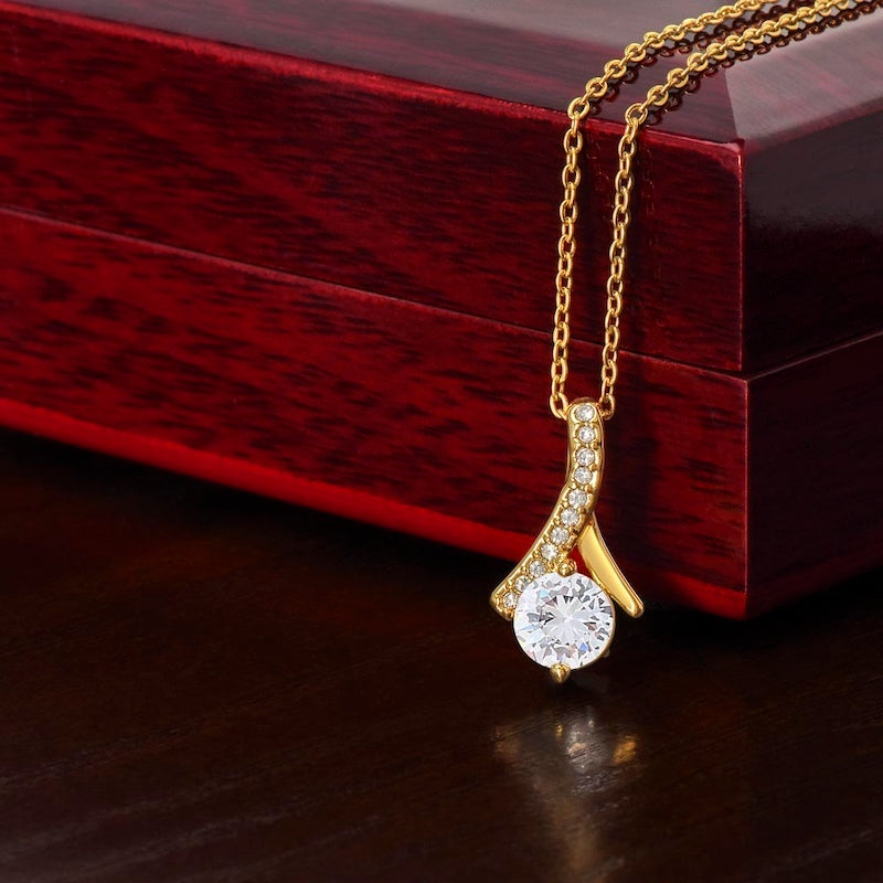 Gold necklace with a zirconia crystal centered pendant on a wooden gift box