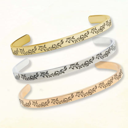 Three gold, silver, and rose gold bangles with leaf patterns on a white background