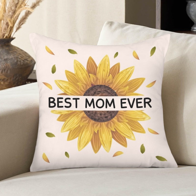 Off-white square decorative pillow cover featuring a bright sunflower design with floating leaves and "BEST MOM EVER" printed across a white banner overlay.   