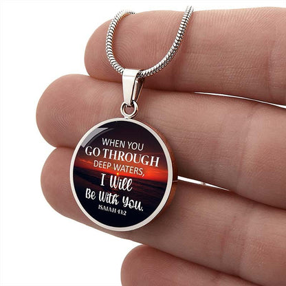 Round silver pendant with a bible verse held between fingers.