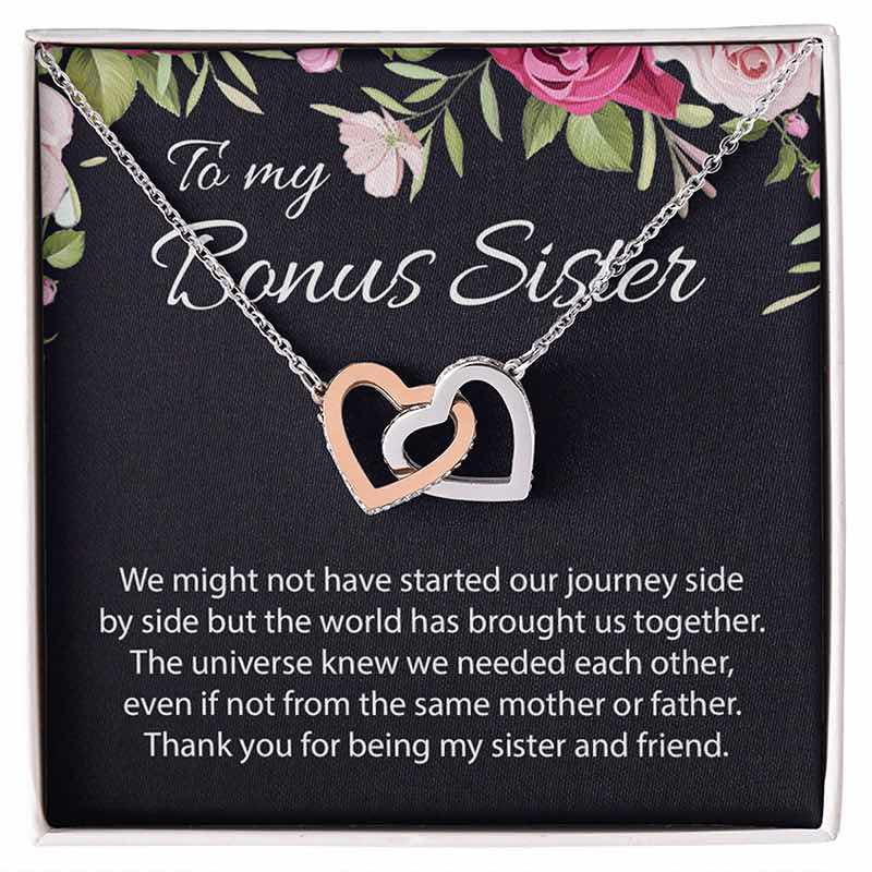 A double-heart pendant necklace with one rose gold heart and one silver heart, displayed on a black gift card with floral accents and the text 'To my Bonus Sister' and a sentimental message.
