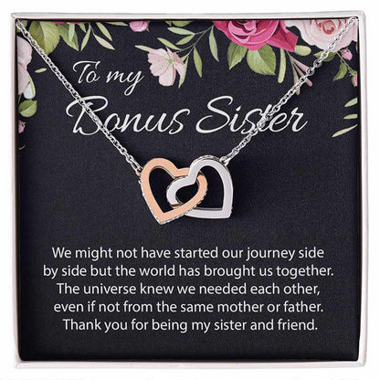A double-heart pendant necklace with one rose gold heart and one silver heart, displayed on a black gift card with floral accents and the text 'To my Bonus Sister' and a sentimental message.
