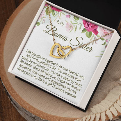 Personalized gift for sister: To My Bonus Sister gold interlocking heart necklace in a gift box on a wooden slice background with a floral message card.   