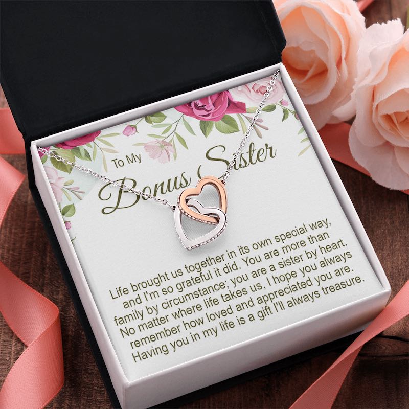To My Bonus Sister interlocking rose gold and silver heart necklace in a gift box with a floral message card, surrounded by pink roses and ribbon.   