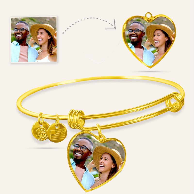 Gold bangle with heart-shaped photo charms featuring a couple, on a light beige background.