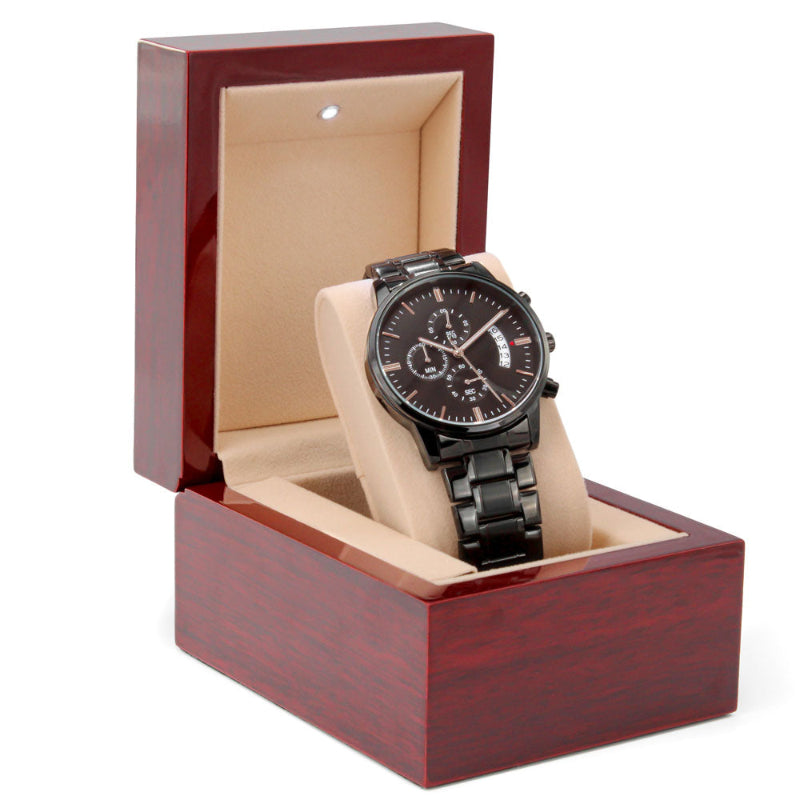 Close-up of a black chronograph watch presented in a Mahogany luxury box.