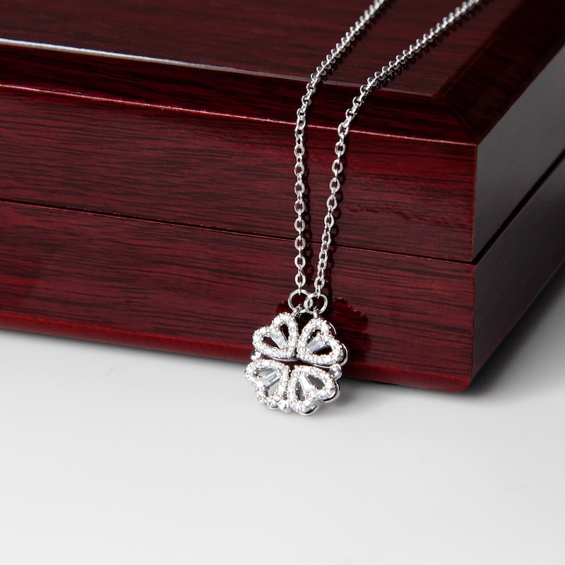 Silver necklace with a clover pendant on a wooden box.