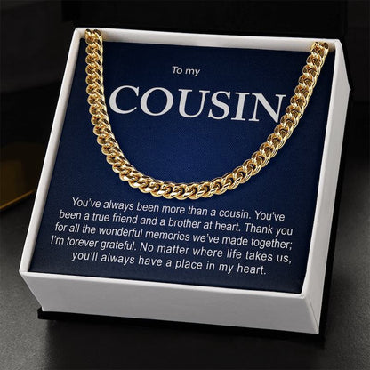 Gold Cuban link chain necklace presented inside an open black gift box resting on a dark surface, featuring a dark blue card titled "To my COUSIN" with a sentimental message.   