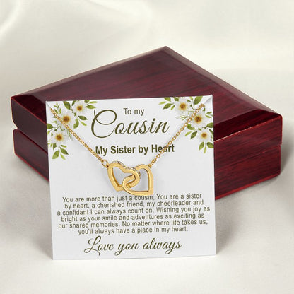 Gold interlocking hearts necklace on a floral cousin message card resting in front of a closed luxury mahogany-style gift box on a white silk background.