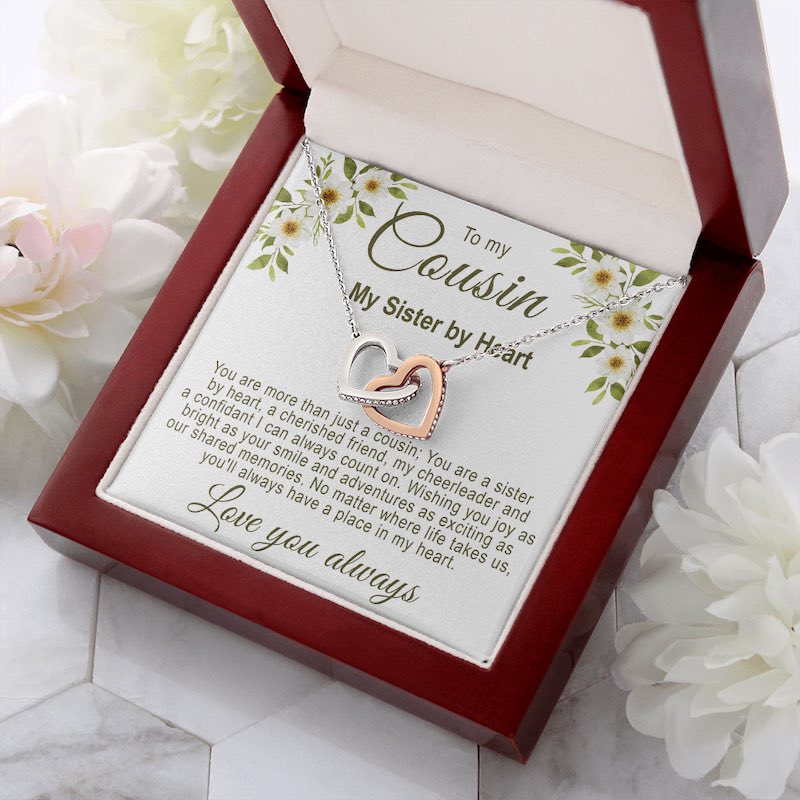 Sentimental gifts for cousin: Interlocking rose gold and silver hearts necklace in a luxury mahogany-style gift box with a floral cousin message card, resting on marble with white floral accents.