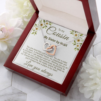 Sentimental gifts for cousin: Interlocking rose gold and silver hearts necklace in a luxury mahogany-style gift box with a floral cousin message card, resting on marble with white floral accents.