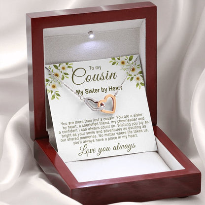 Christmas gifts for your cousin: Illuminated mahogany-style gift box resting on a white silk background, displaying an interlocking rose gold and silver hearts necklace with a floral cousin message card.