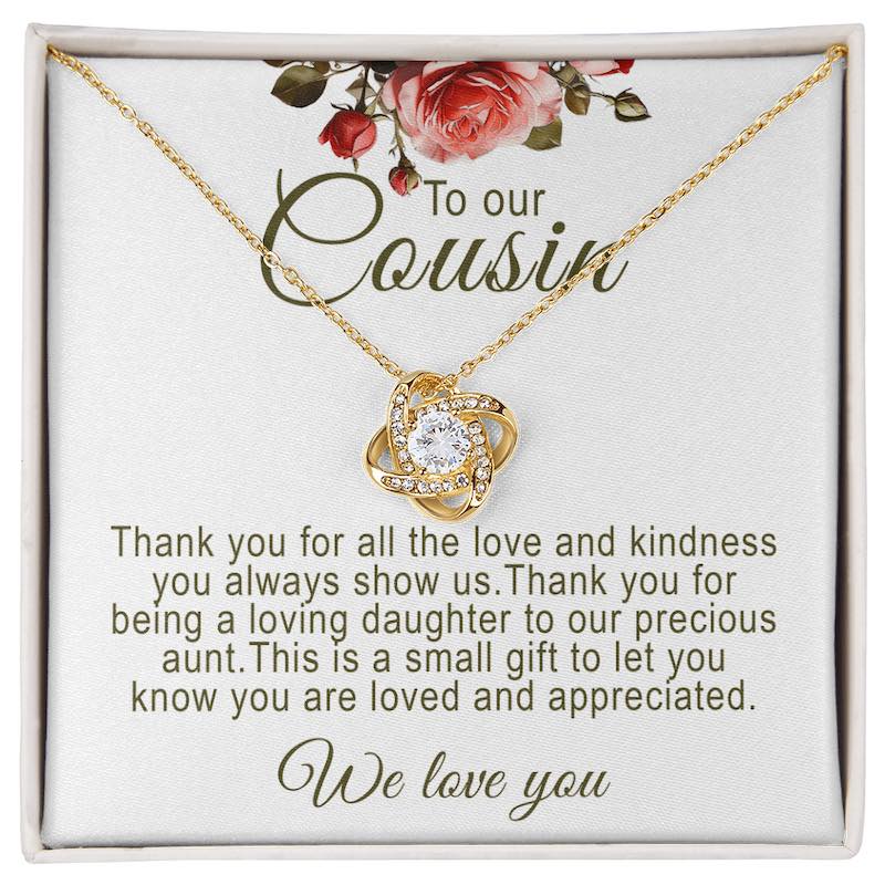 Gold love knot pendant necklace with a round central crystal set inside a white gift box with red rose artwork and a message card titled "To our Cousin".   