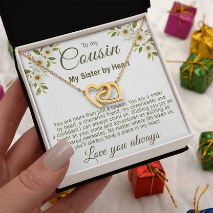 Hand holding a white gift box showcasing a gold interlocking hearts necklace with a floral cousin message card, surrounded by small wrapped gift boxes.
