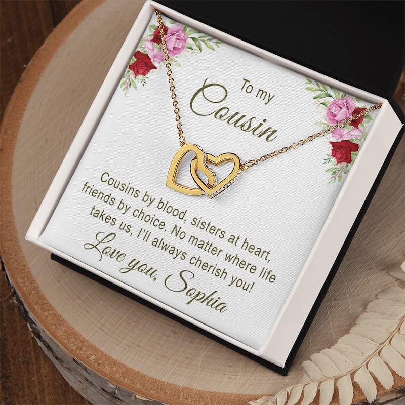 Gold necklace with interlocking hearts displayed on a white and floral designs with personalized text for cousin, in a two tone box.