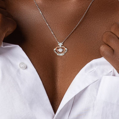 Necklace with a crown heart-shaped pendant worn by a person in a white shirt.