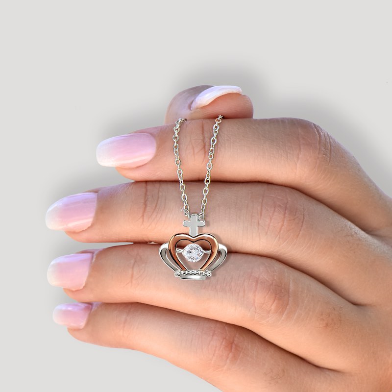Crown heart-shaped necklace with a cross on a hand with pink nail polish against a light gray background