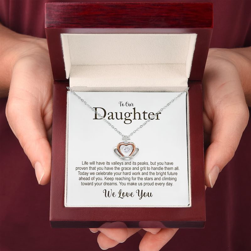 Necklace with crown heart design in a wooden box held by hands, featuring a message card for a daughter.