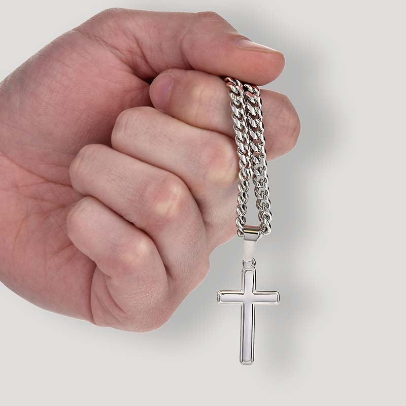 Hand holding a silver chain with a cross pendant against a light background