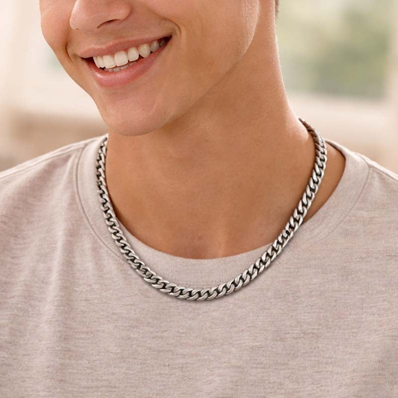 Person wearing a silver cuban link chain necklace with a blurred background