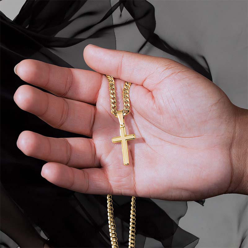 Gold cross necklace held in a hand against a neutral background