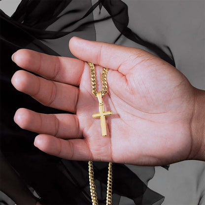 Gold cross necklace held in a hand against a neutral background