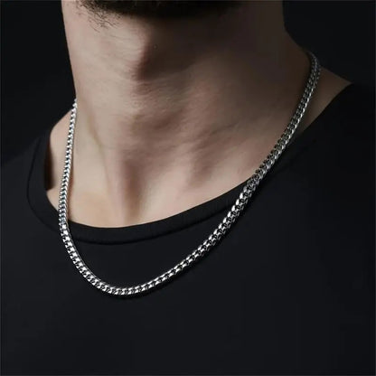 Close-up of a man wearing a silver Cuban link chain necklace over a black t-shirt.   