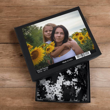 Open custom photo puzzle box on a wooden surface filled with loose black-backed puzzle pieces.