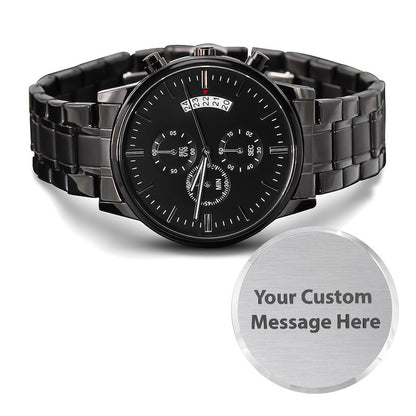 A black stainless steel analog watch with a multi-dial design and a day/date window, shown alongside a circular silver customizable badge that reads 'Your Custom Message Here'.