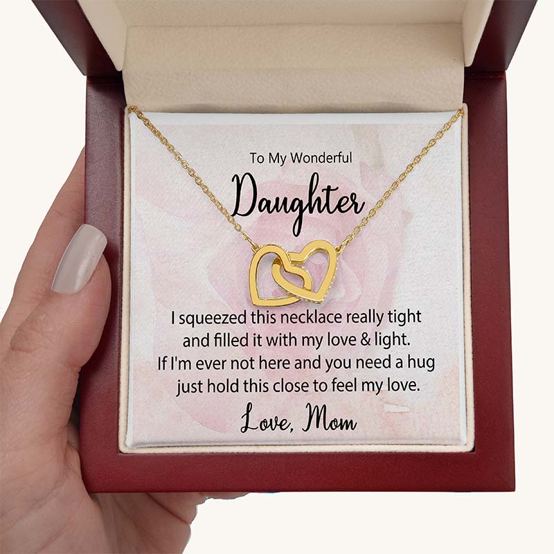 Gold interlocking heart necklace displayed in a gift box with a heartfelt daughter message card from Mom, held in hand against a white background