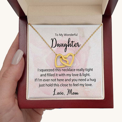 Gold interlocking heart necklace displayed in a gift box with a heartfelt daughter message card from Mom, held in hand against a white background