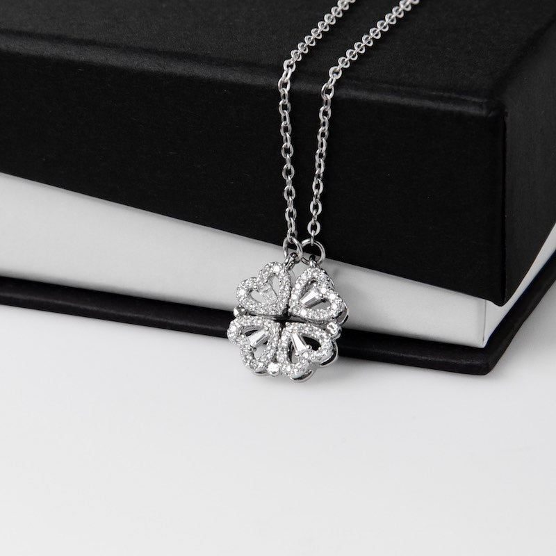 Silver necklace with a clover pendant, featuring four hearts on a white and black gift box.