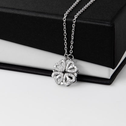 Silver necklace with a clover pendant, featuring four hearts on a white and black gift box.