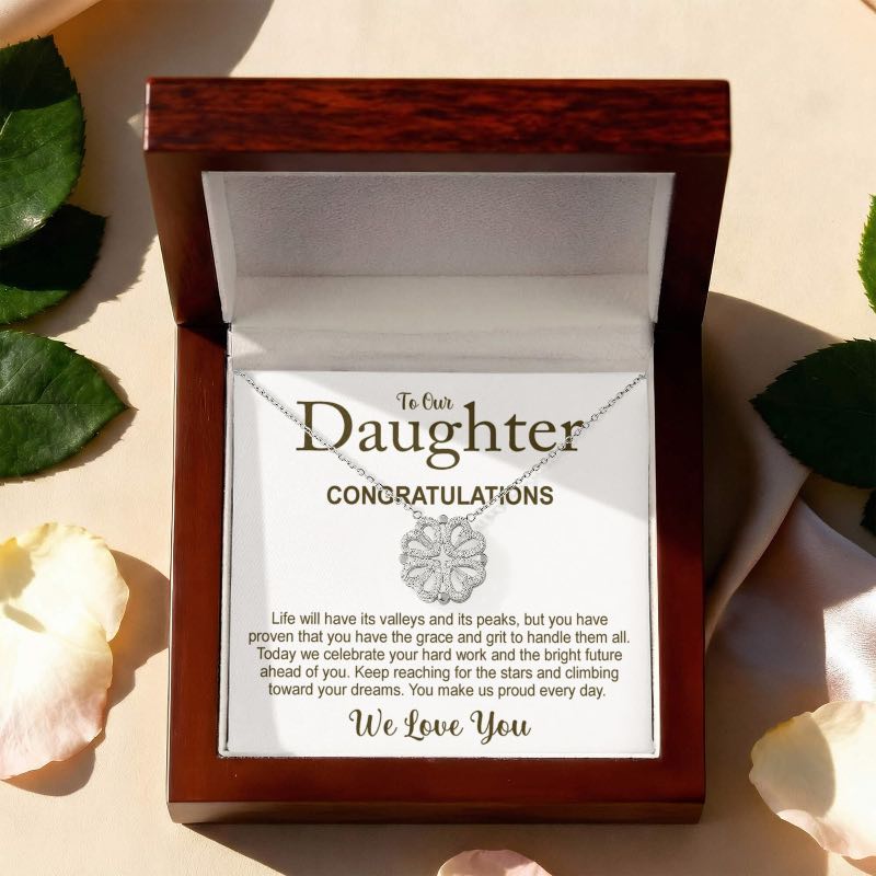 Necklace in a wooden box with a message card for a daughter, surrounded by leaves and flowers.