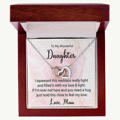 Two-tone interlocking heart necklace displayed in a luxury mahogany gift box with a heartfelt daughter message card from Mom against a soft pink floral background.