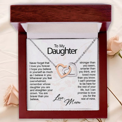 A heart-shaped double necklace with one rose gold heart and one silver heart on a printed message card, presented inside an open dark wood gift box with a floral background.