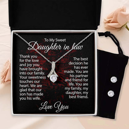 Silver ribbon pendant necklace displayed in a gift box with a heartfelt daughter-in-law message card, matching cubic zirconia stud earrings in a black velvet pouch, against a soft blush rose background.