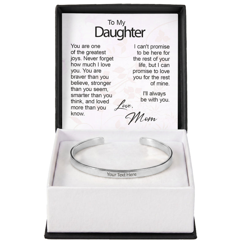 A silver custom-engraved cuff bracelet with "Your Text Here" placeholder text, set inside an open gift box featuring a printed sentiment card titled "To My Daughter" signed "Love, Mom".