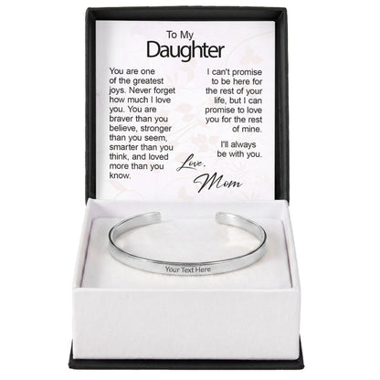 A silver custom-engraved cuff bracelet with "Your Text Here" placeholder text, set inside an open gift box featuring a printed sentiment card titled "To My Daughter" signed "Love, Mom".