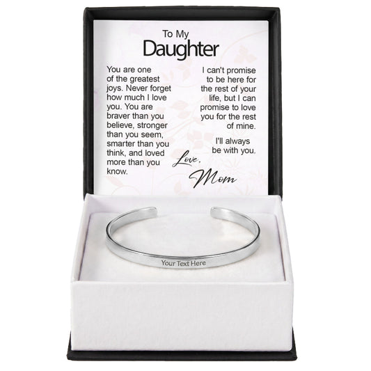 A silver custom-engraved cuff bracelet with "Your Text Here" placeholder text, set inside an open gift box featuring a printed sentiment card titled "To My Daughter" signed "Love, Mom".
