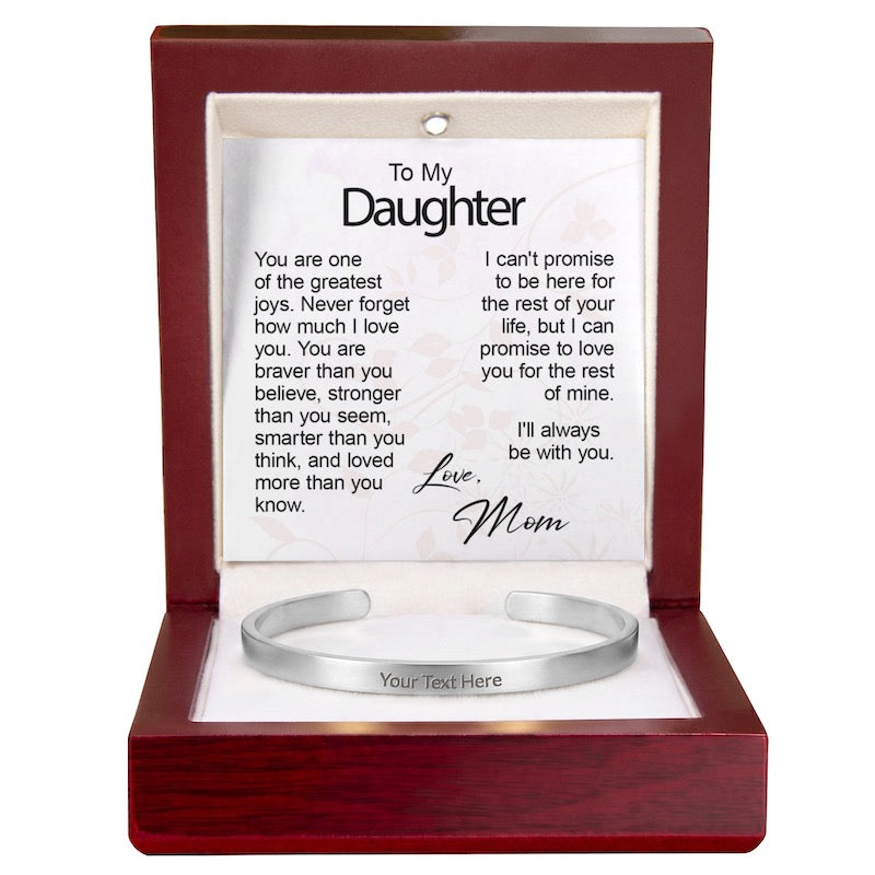 A polished silver cuff bracelet engraved with "Your Text Here" resting in an open wooden gift box with built-in LED lighting, showcasing a "To My Daughter" message card from Mom.