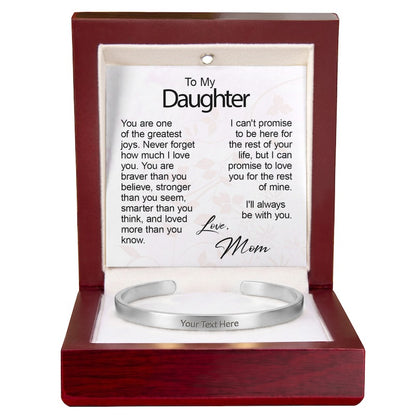 A polished silver cuff bracelet engraved with "Your Text Here" resting in an open wooden gift box with built-in LED lighting, showcasing a "To My Daughter" message card from Mom.