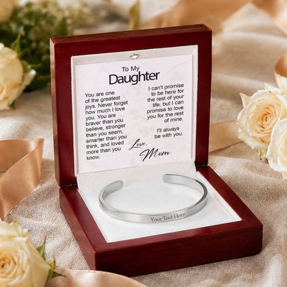 Personalized silver cuff bracelet with "Your Text Here" sample engraving, presented in an open wooden gift box resting on textured beige silk beside white roses, featuring a "To My Daughter" card from Mom.   