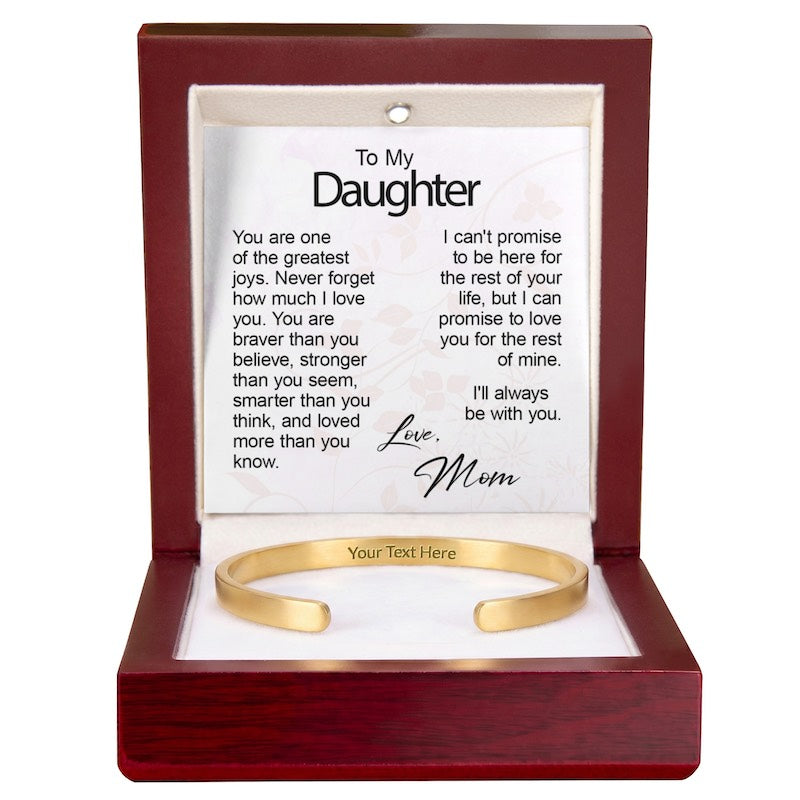Gold cuff bracelet with inside engraving displayed in an open wooden gift box with an illuminated top interior and a printed "To My Daughter" message card signed "Love, Mom."   
