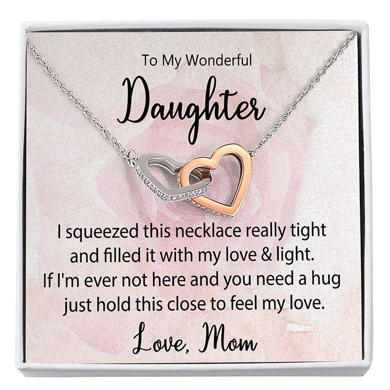 Daughter Interlocking Hearts Necklace: Two-tone interlocking heart necklace displayed in a gift box with a heartfelt daughter message card from Mom against a soft pink floral background.